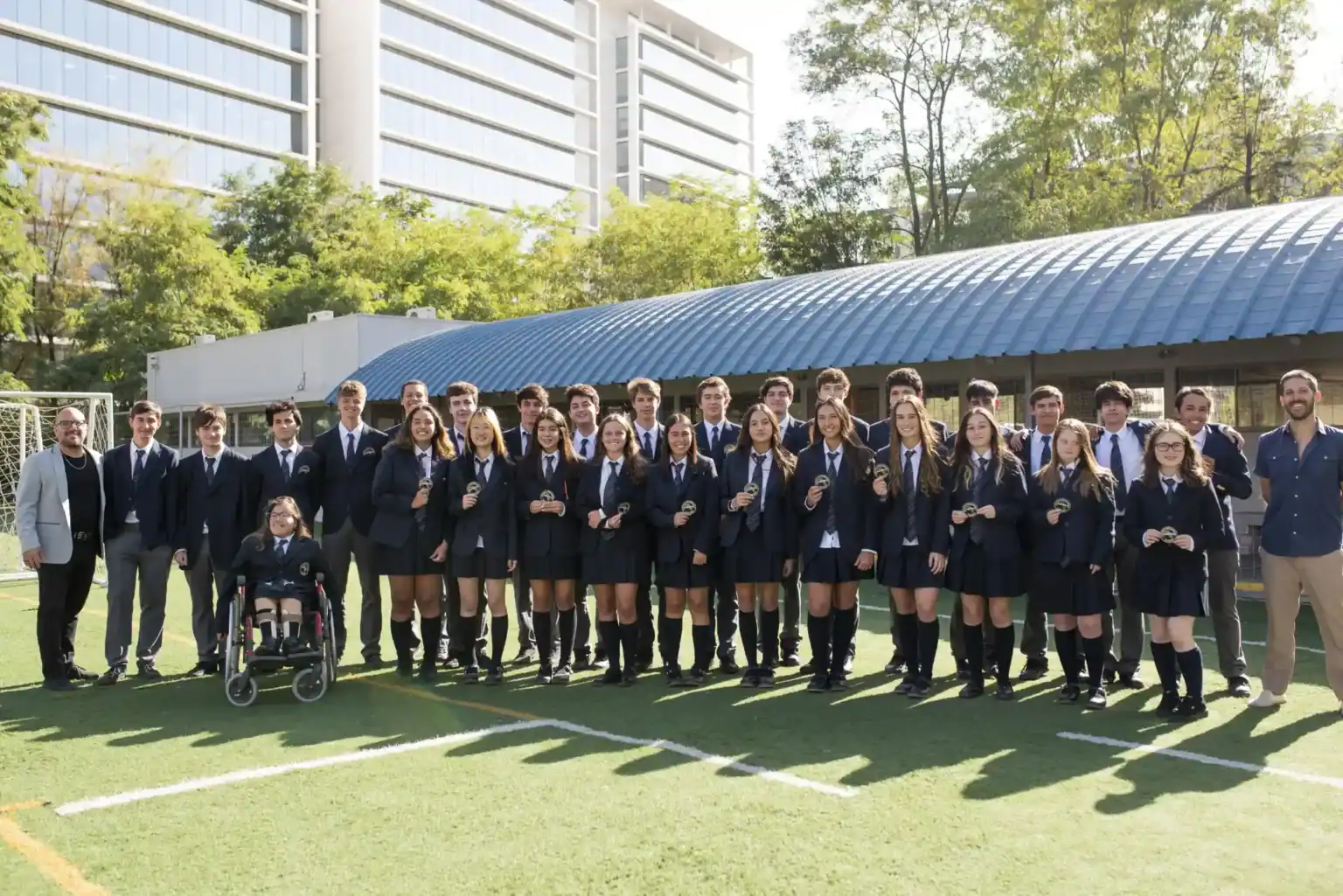 正式な制服を着た生徒たちが、ワールド・スクールの優秀な学業を象徴する賞状を手に、スポーツフィールドでポーズをとっている。.