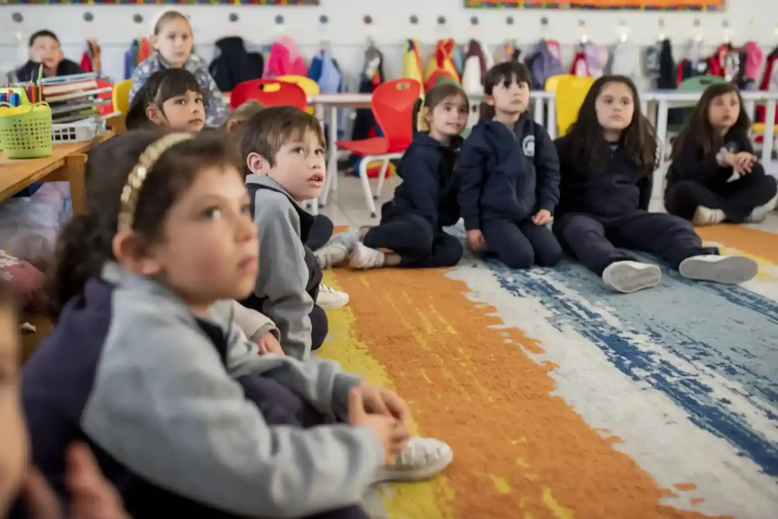 ワールドスクールのオンライン授業で教室のカーペットに座る生徒たち。.