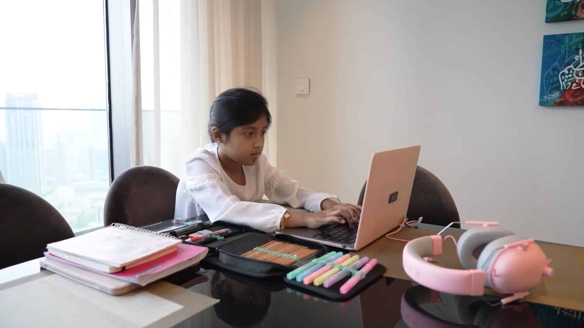 Teen girl studying online at home, using laptop, with school supplies and headphones.