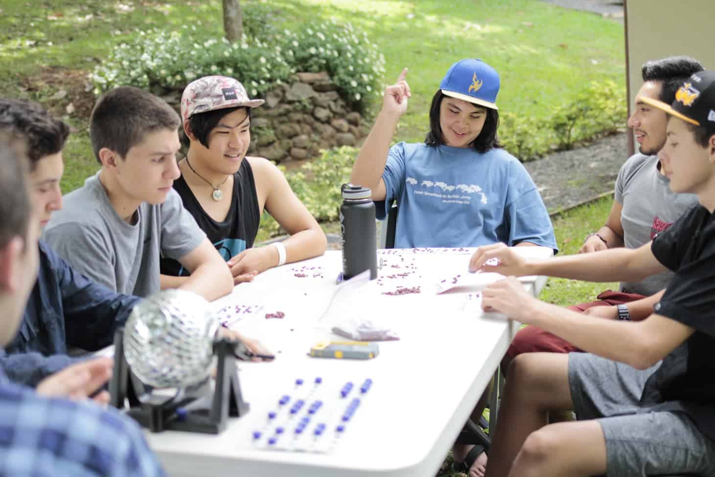 Diverse students collaborating outdoors at a school table, engaging in educational activities.