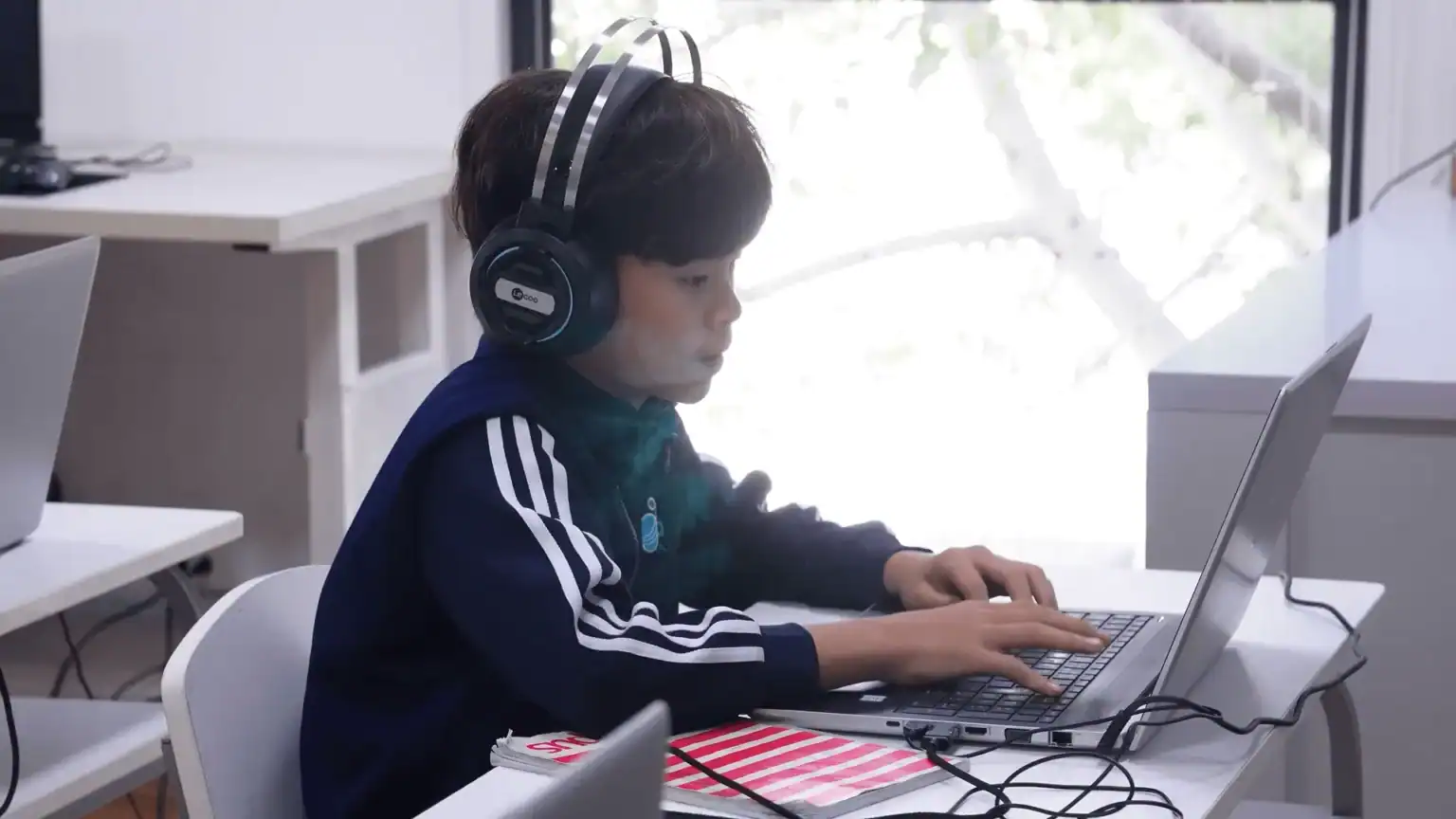 Młody uczeń uczący się ze słuchawkami na laptopie w nowoczesnej klasie, będącej częścią innowacyjnego środowiska edukacyjnego World Schools.