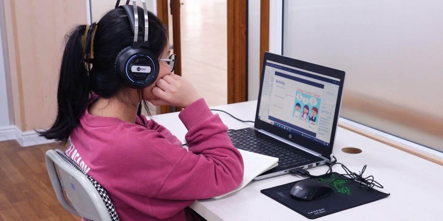 Dziewczyna ucząca się online ze słuchawkami, laptopem i treściami edukacyjnymi na ekranie w domu.