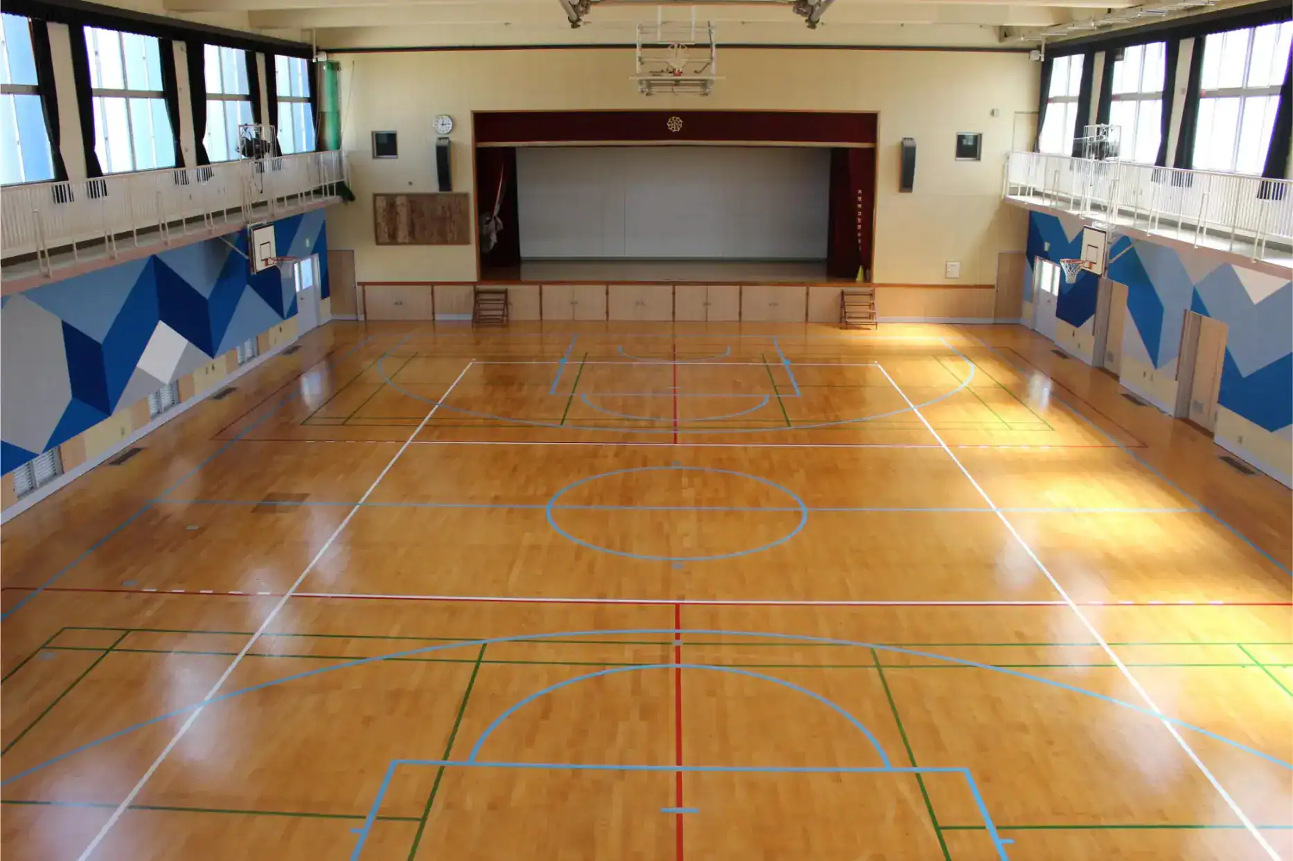 Bright indoor gymnasium with colorful court markings, stage, and sports facilities, ideal for school sports activities.