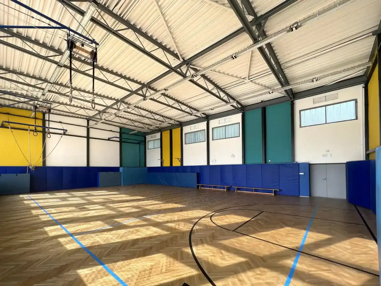 Bright indoor gymnasium with wooden flooring and colorful wall panels, perfect for student sports and physical activities.