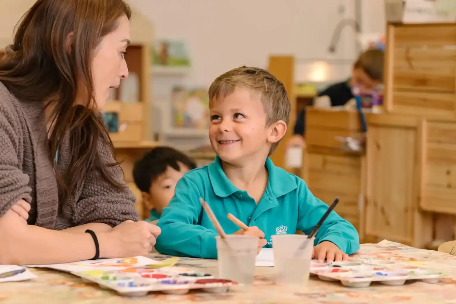 Bright young boy smiling and talking with teacher in a classroom setting for kids education.