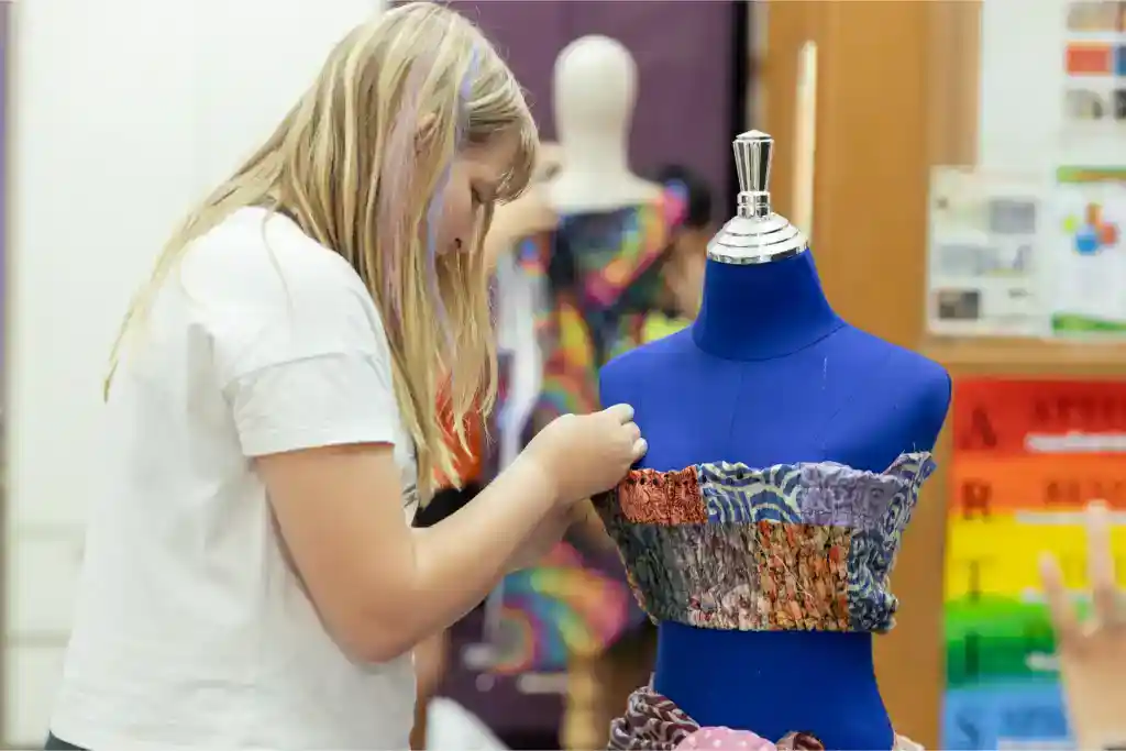 Bright young student working on fabric design at fashion school mannequin, focusing on creative skills training.