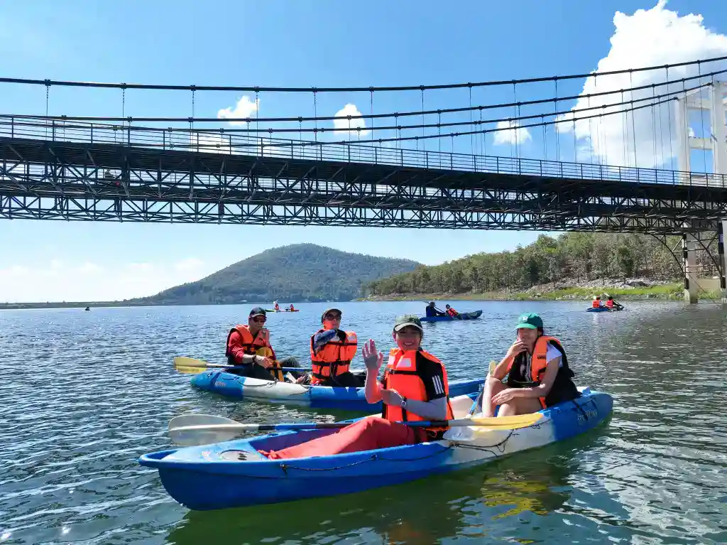 Kayaking on a scenic river with students under a bridge, promoting outdoor education and adventure activities.