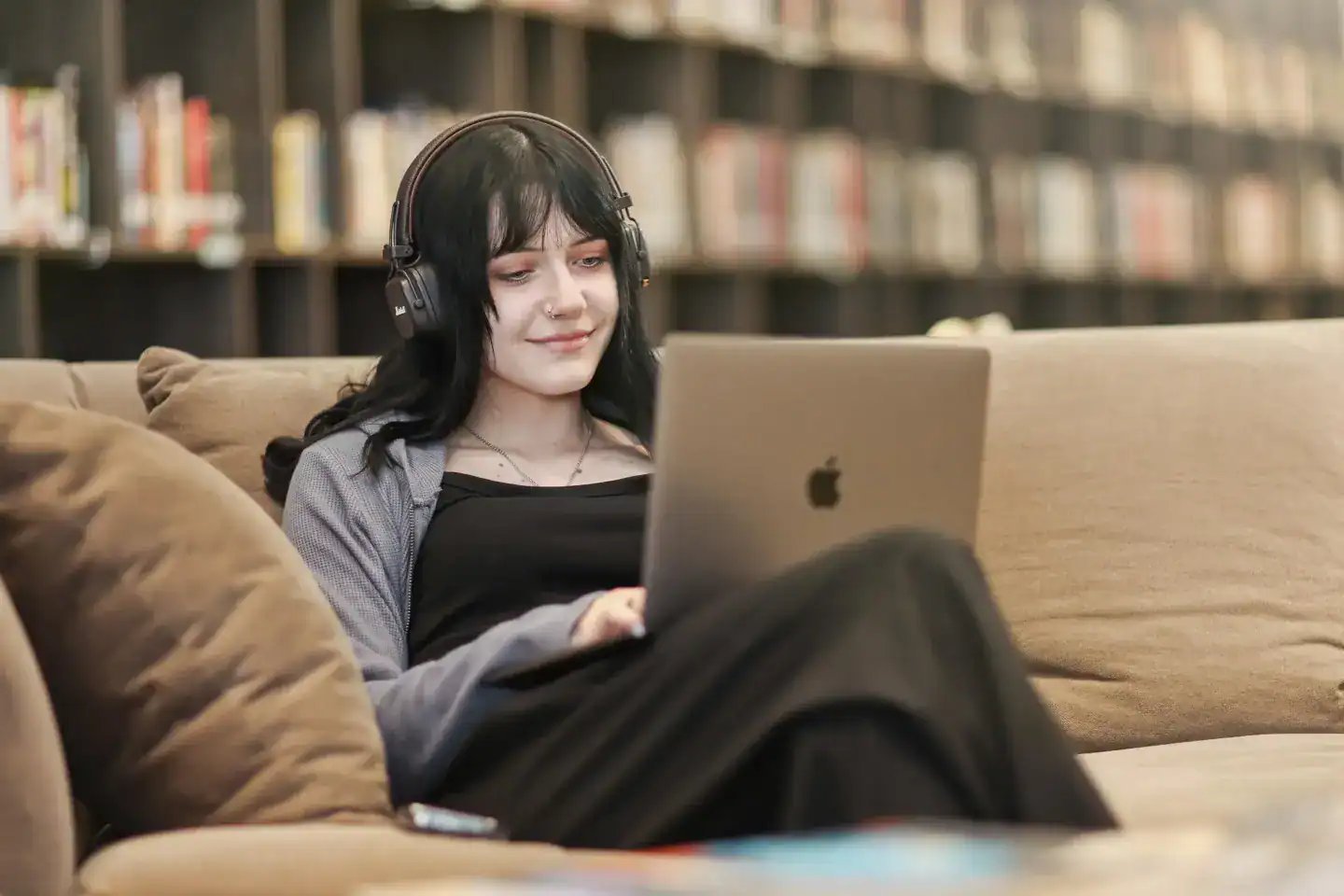 Young woman with headphones studying on a laptop in a library setting.