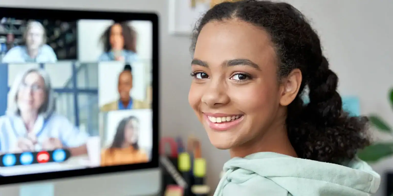 Bright African-American girl smiling during a virtual online class, using a computer for education, diverse students learning remotely.