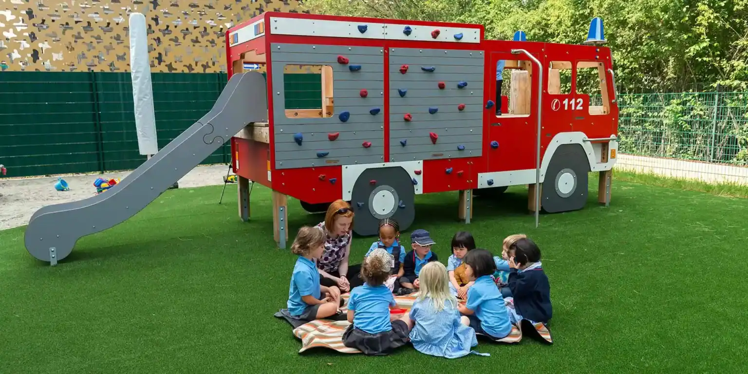 Kids playing on a fire truck-themed playground structure at an international school.