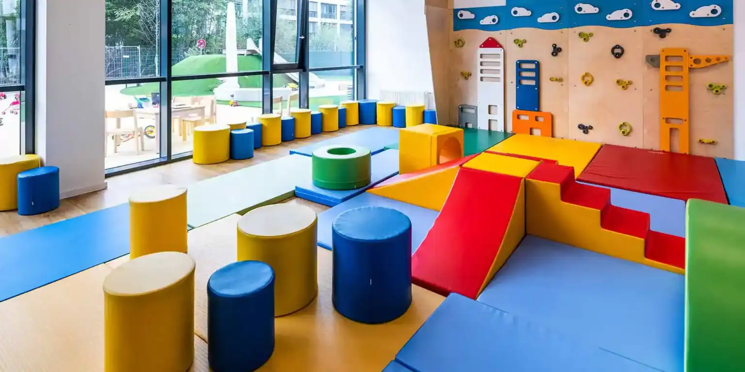Bright colorful indoor children's play area with climbing wall and soft mats for early childhood education.