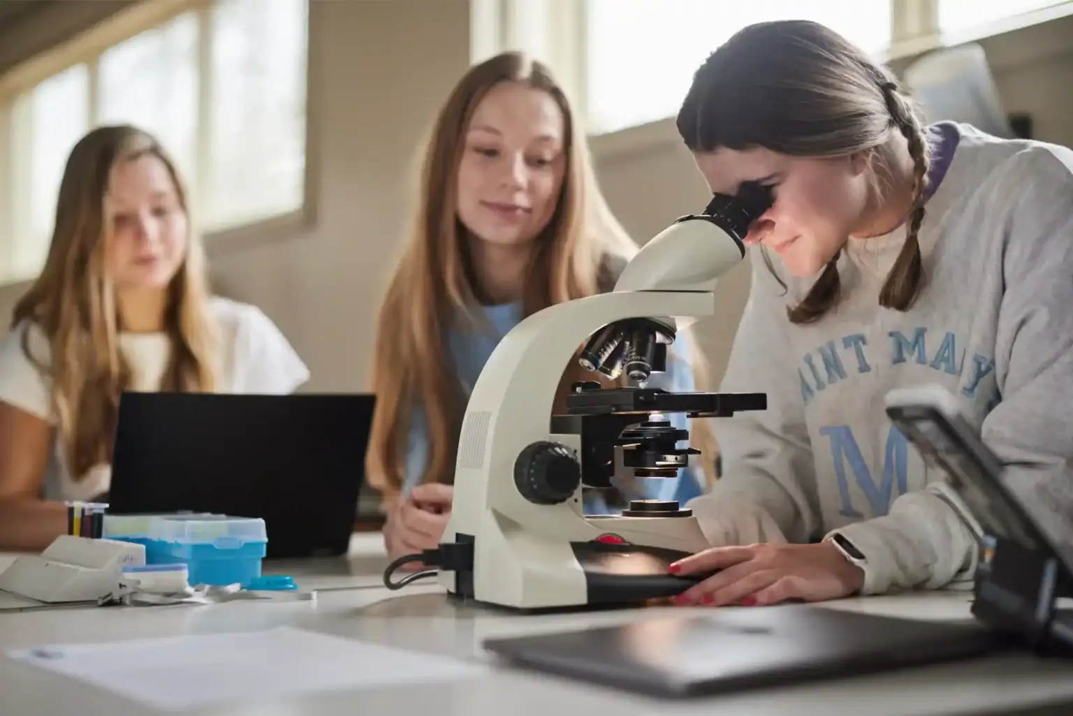 High school girls conducting science experiments with microscope in classroom, focusing on STEM education.