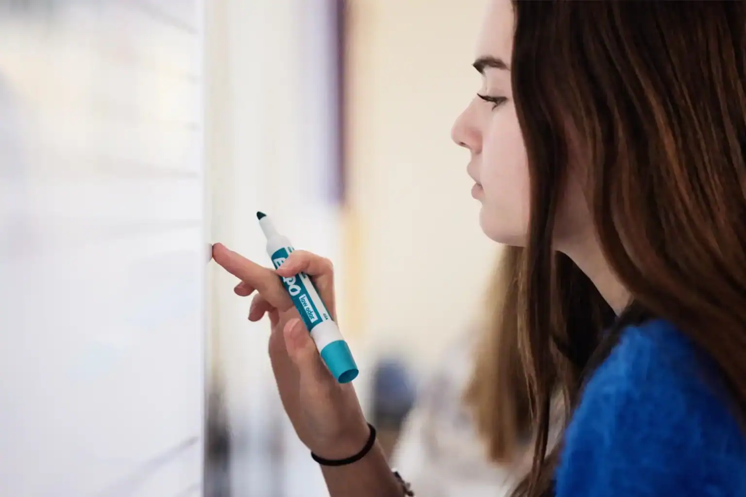 Young female student writing on whiteboard at school, focusing on education and learning.