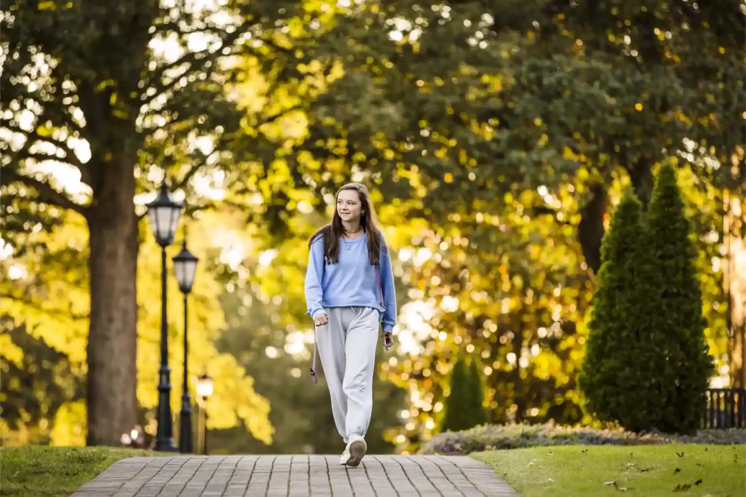 Students walking outdoors in a peaceful, green school campus setting with trees and warm sunlight.