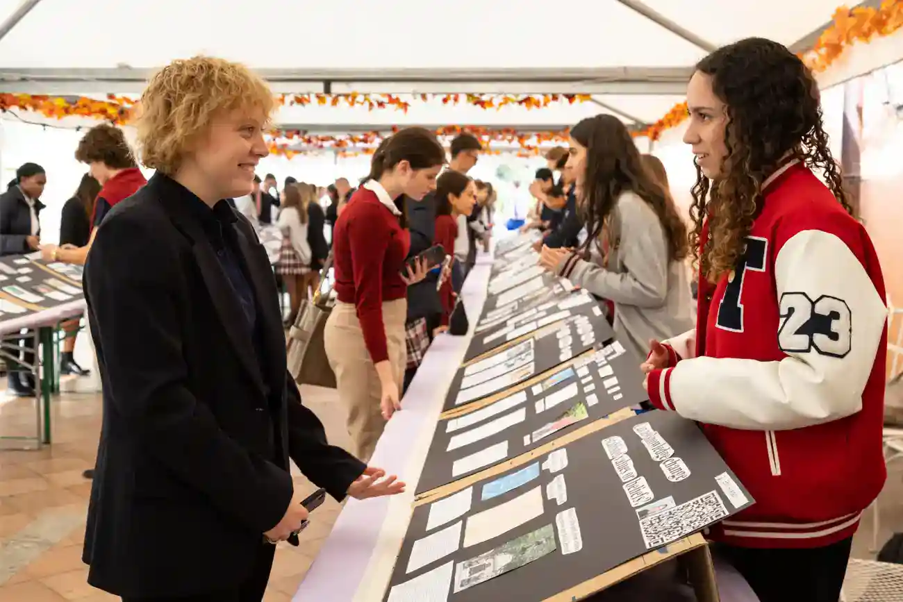 This Year at TASIS: 2023 26 Diverse students examining project displays at a school fair, showcasing academic excellence and student engagement.