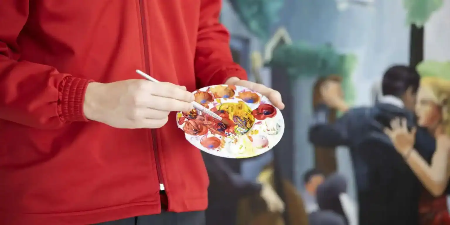 Brightly dressed artist mixing vibrant colors on a palette for creative art projects at a school.