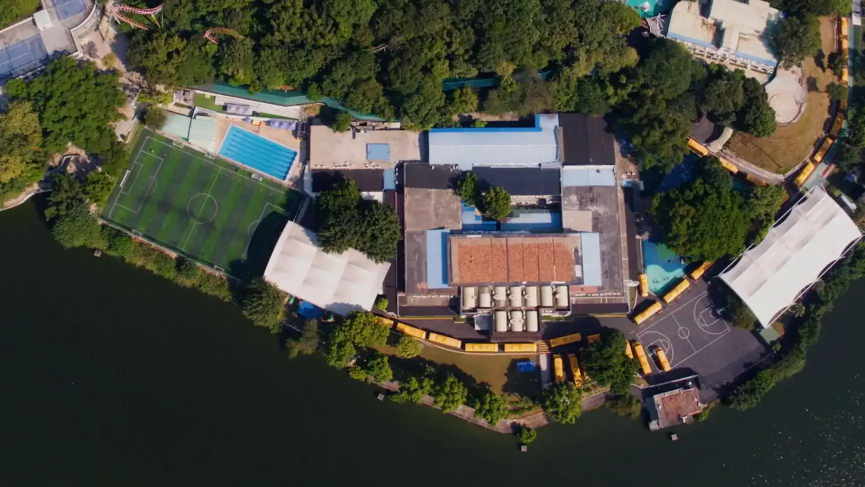 Aerial view of an international school campus with sports fields, swimming pool, and surrounding greenery.