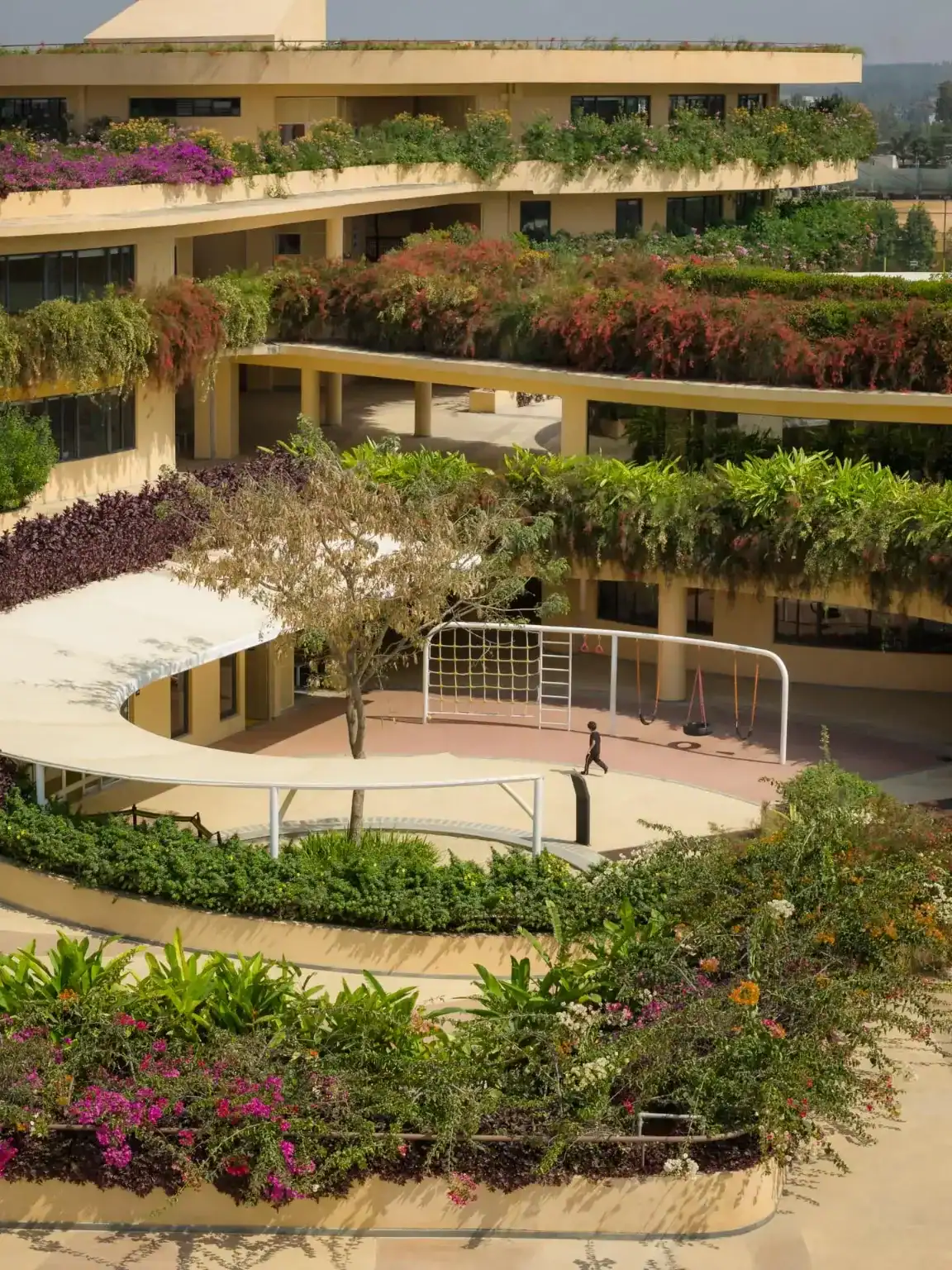 Modern school building with lush green rooftop gardens and outdoor sports area.