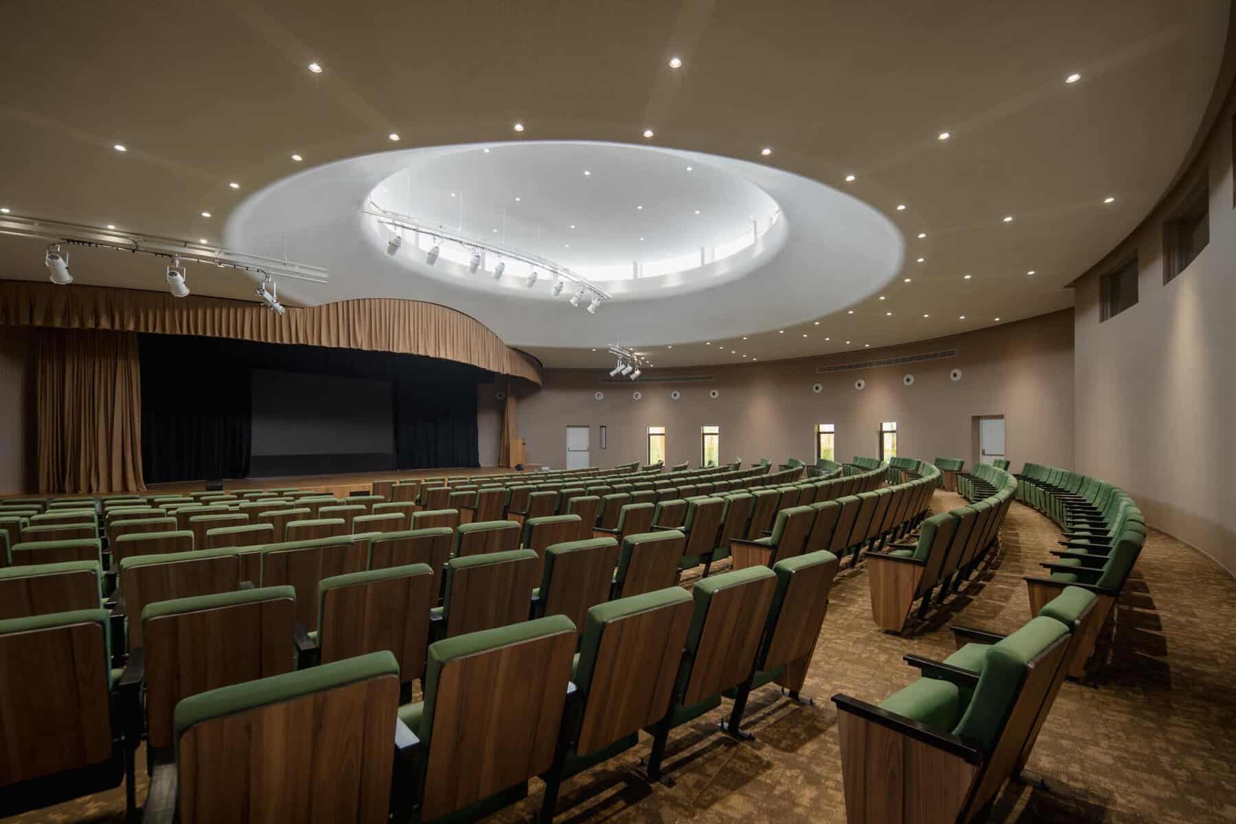 Modern auditorium with tiered seating and a circular skylight ceiling.