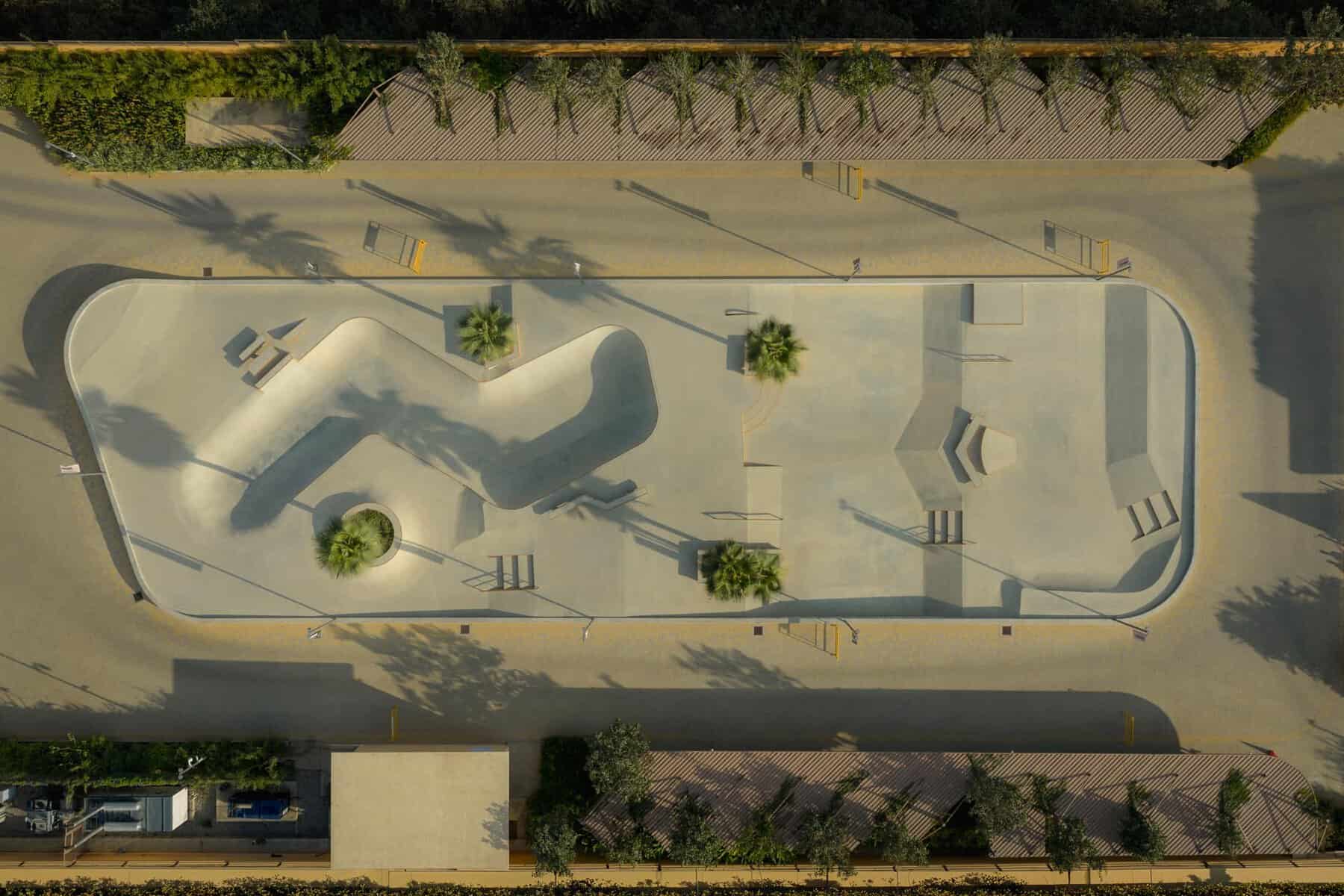 Aerial view of a modern skatepark with ramps and seating areas in an urban setting.