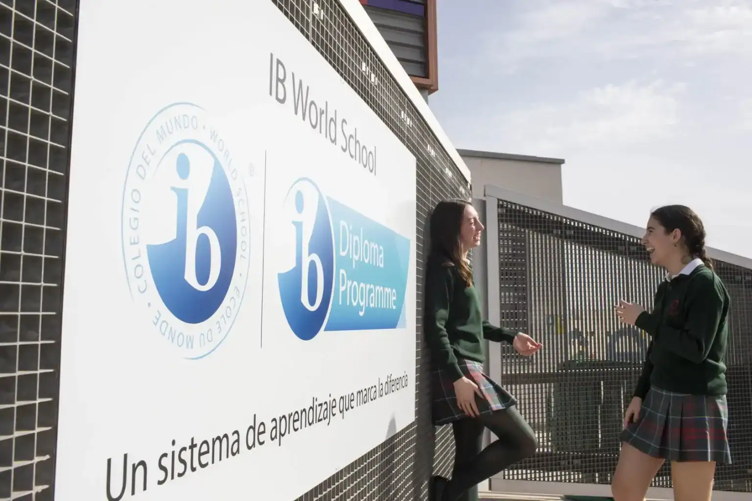 IB World School students discussing on campus with IB diploma program sign in background.