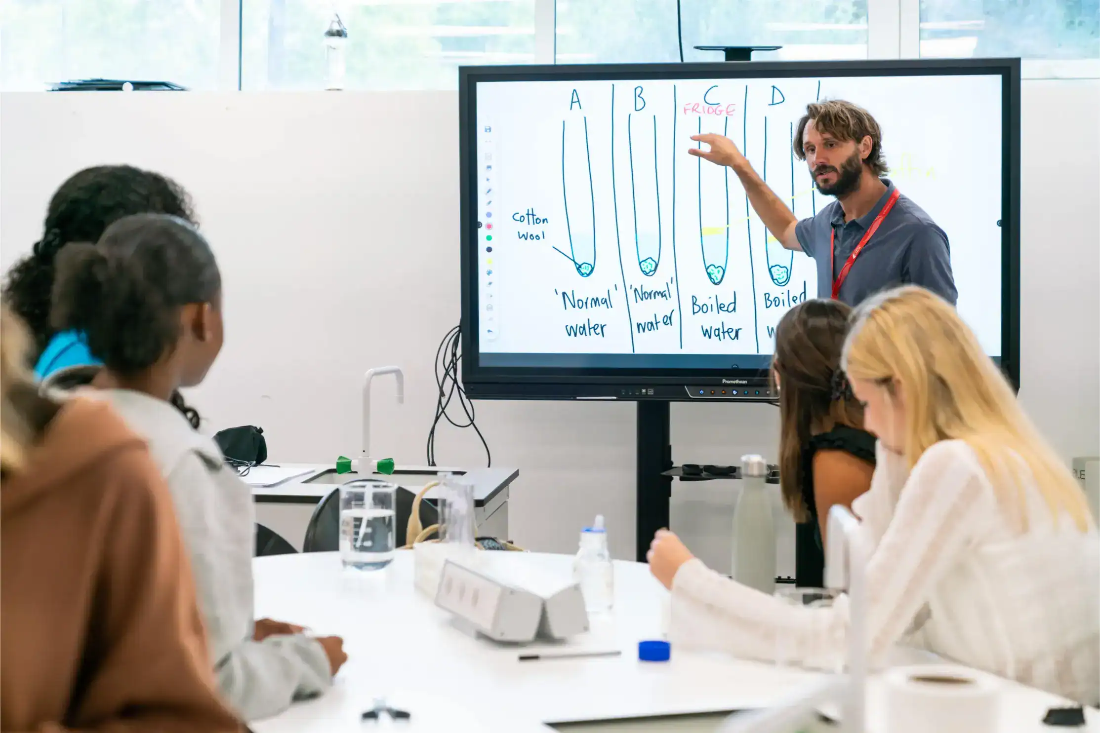 Colorful classroom with teacher explaining science experiment on smartboard, students engaged.