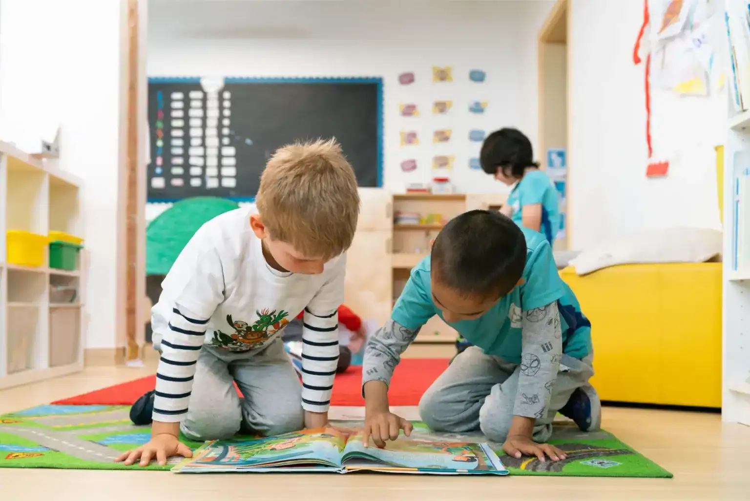 Children reading a book together in a vibrant classroom setting with educational decorations.