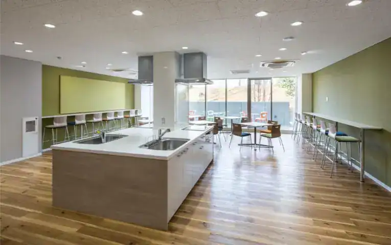 Bright modern school cafeteria with natural light, wooden floors, and seating areas for students.
