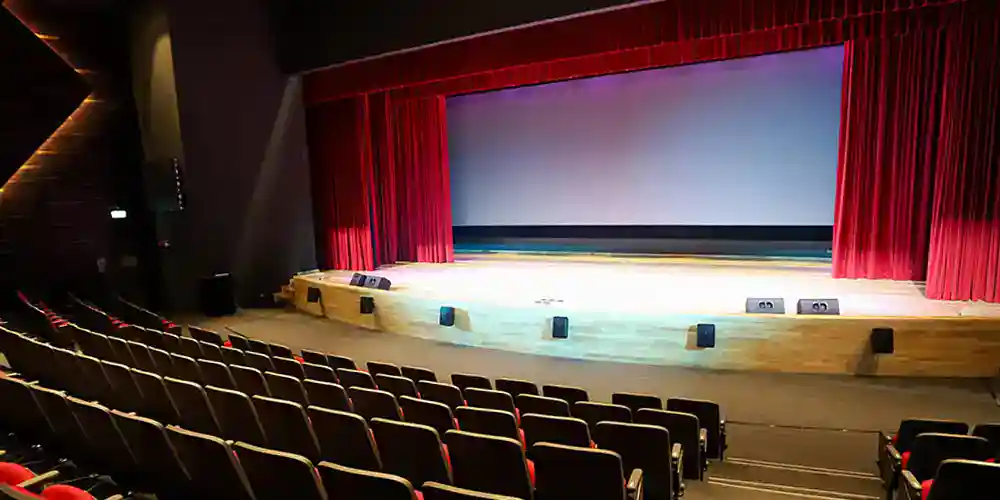 A theater stage with red curtains and empty seats, ideal for school performances and events.