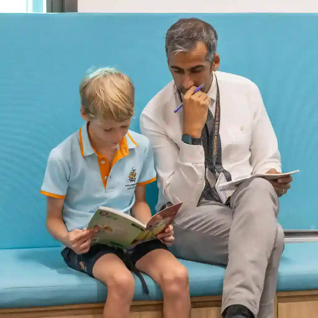 Dedicated teacher assisting a young student with reading in a World Schools educational environment.