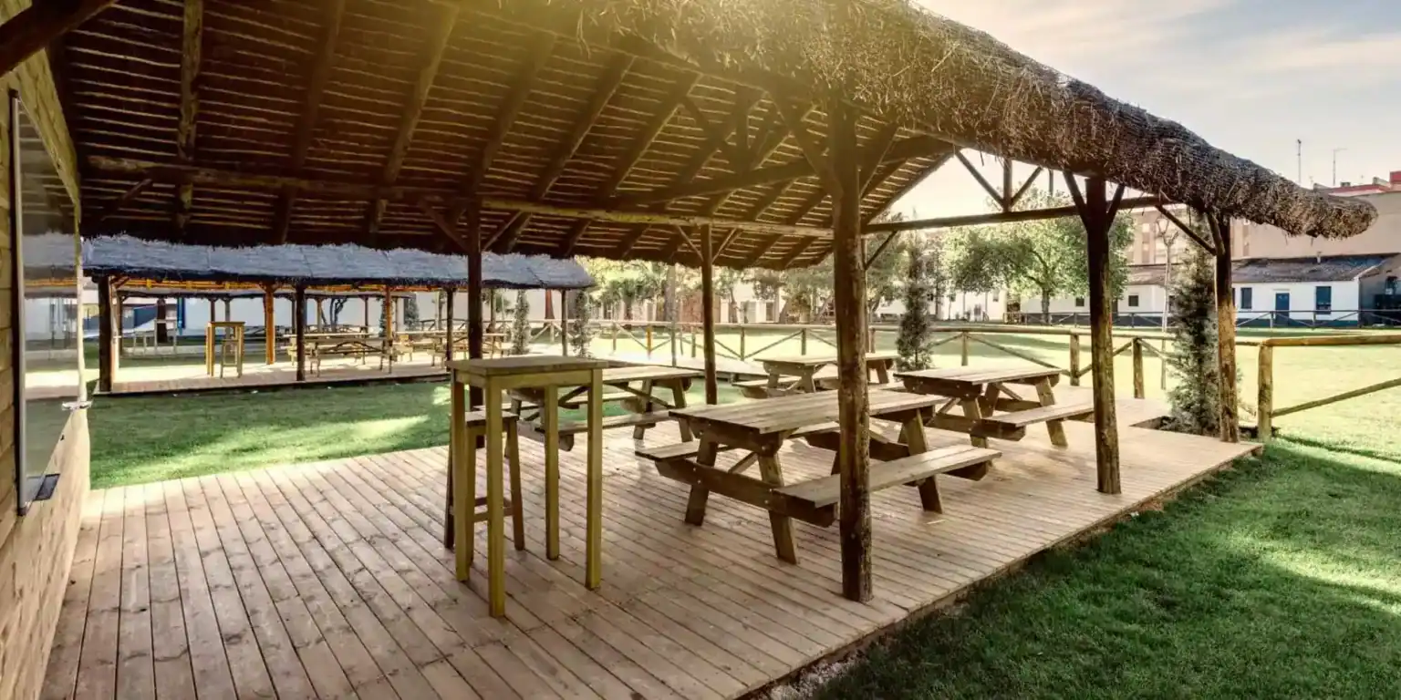 푸른 잔디와 나무로 둘러싸인 나무 테이블과 벤치가 있는 야외 학교 파빌리온. 월드스쿨을 위한 완벽한 학습 환경입니다.