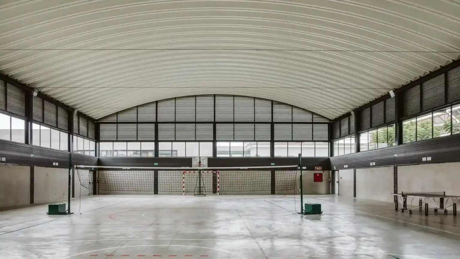 Indoor sports gymnasium at a modern school facility with volleyball court and large windows.