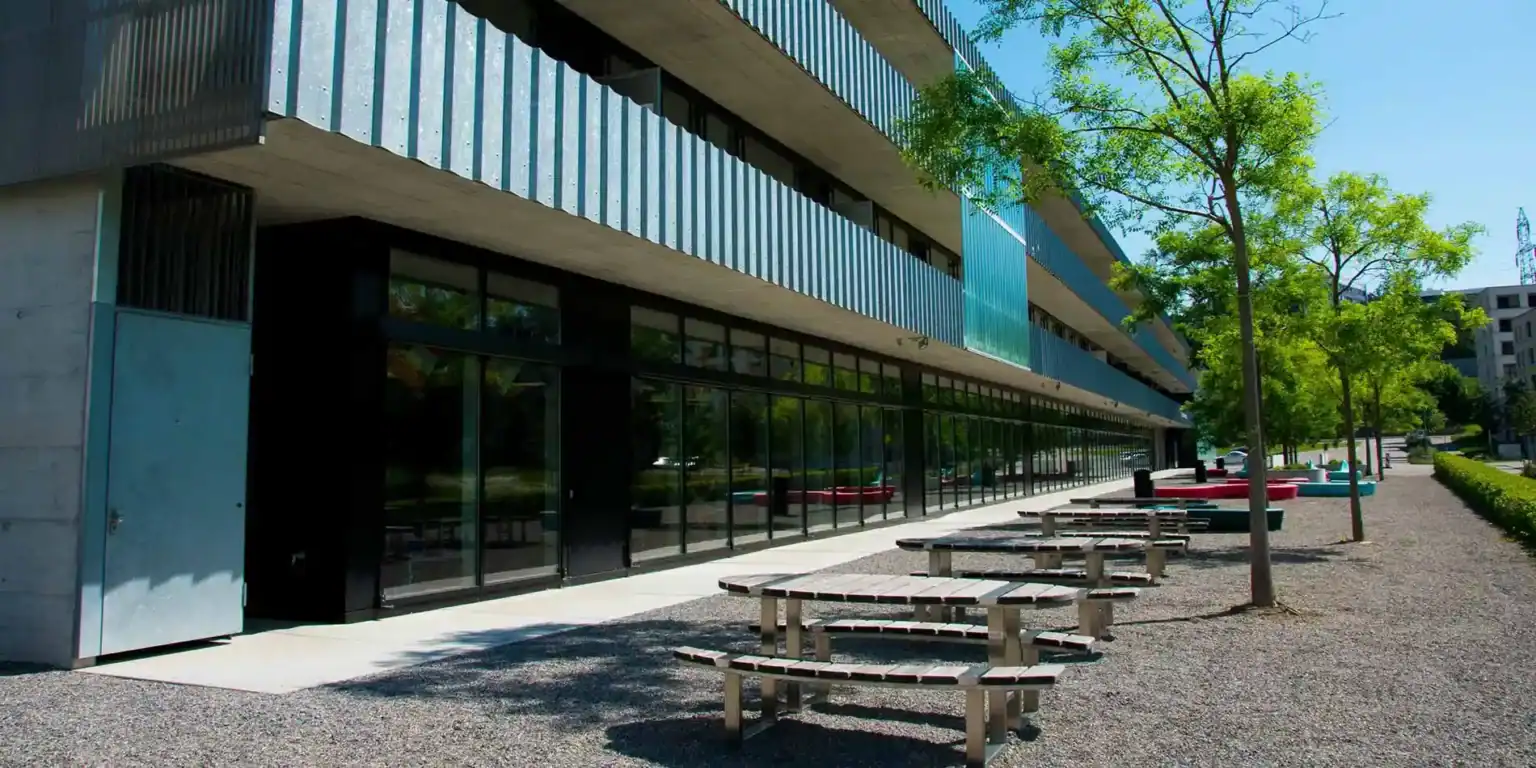 Modern school building with outdoor seating area and green trees for a sustainable learning environment.