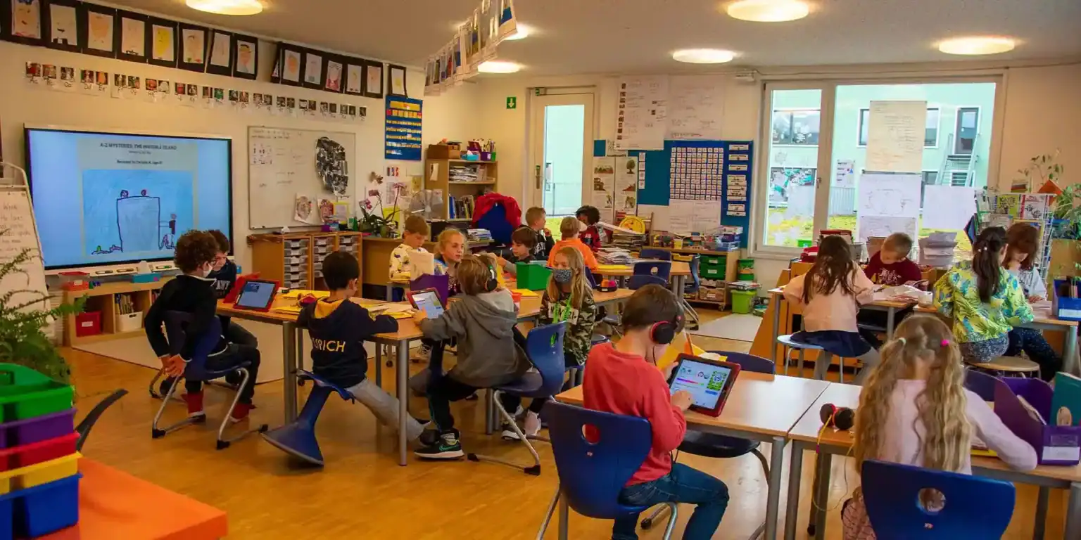 Bright modern classroom with engaged students using tablets, fostering innovative learning at an international school.