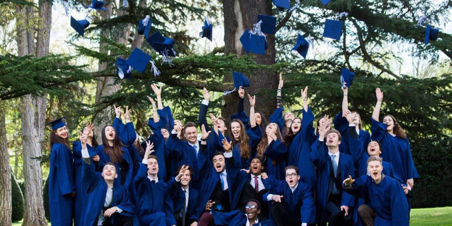 Graduating students in blue gowns celebrating outdoors at a graduation ceremony.