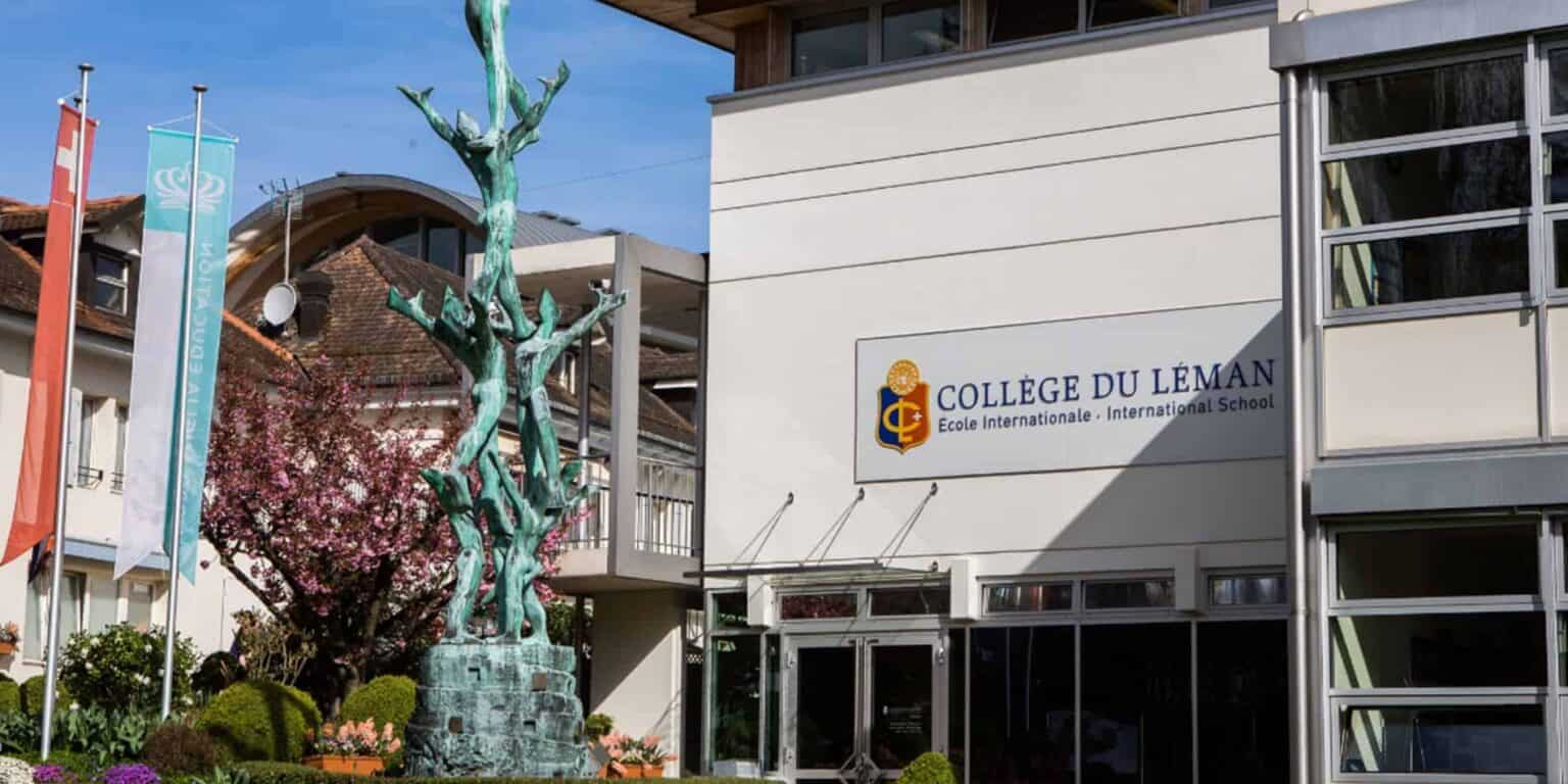 Modern international school building with colorful flags, a statue, and blooming trees, part of Collège du Léman educational campus.