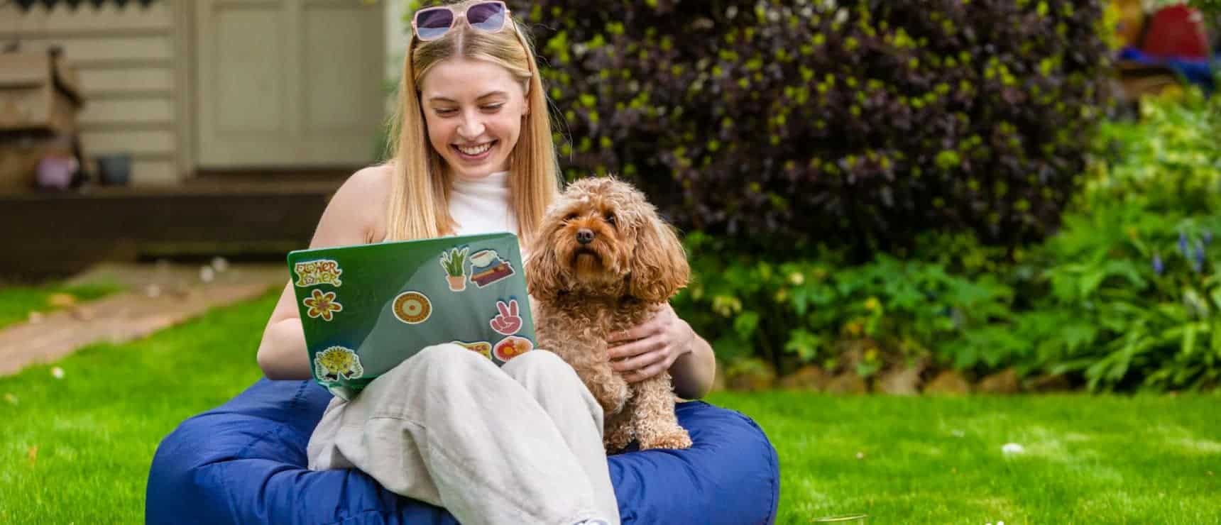 Relaxed student studying outdoors with her dog in a garden, promoting outdoor learning and well-being.
