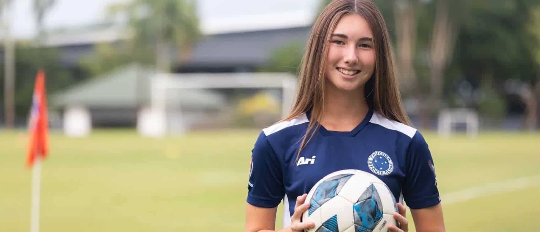 Young female soccer player holding ball on field at World Schools sports event.