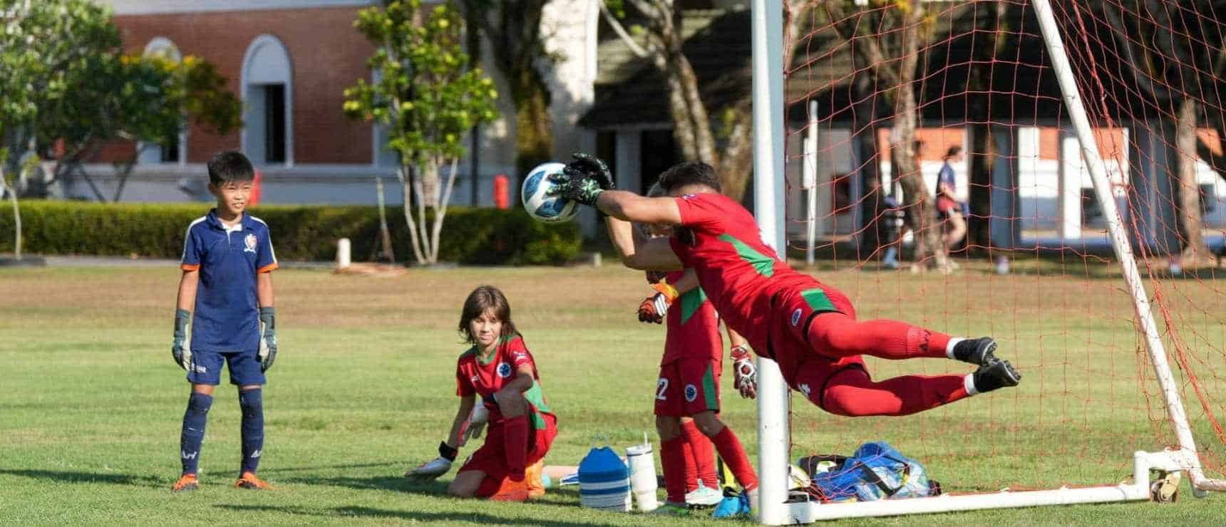 Young soccer goalkeeper in action during match at an international school sports field.