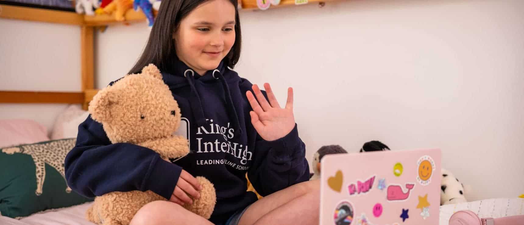 Cute girl engaging in online learning while holding a teddy bear, representing innovative education at world schools.
