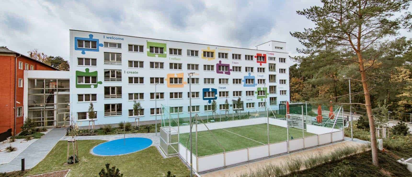Bright modern school building with colorful puzzle-piece design and sports area, ideal for international student education.