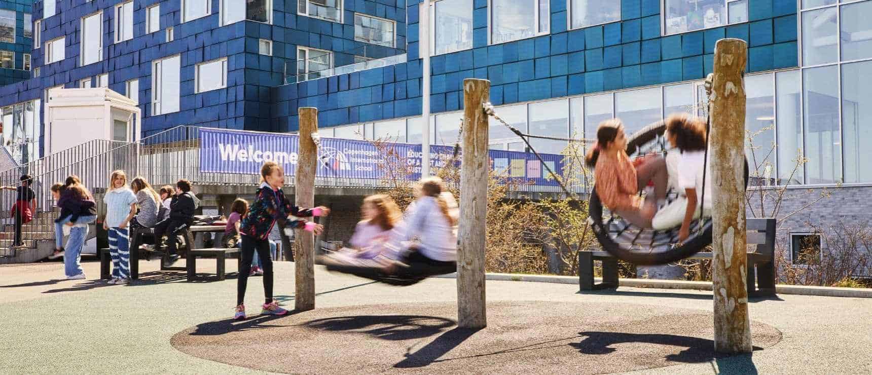Leadership Opportunity: Director Position at Copenhagen International School 6 Children playing on swings and socializing outside a modern school building during daytime.