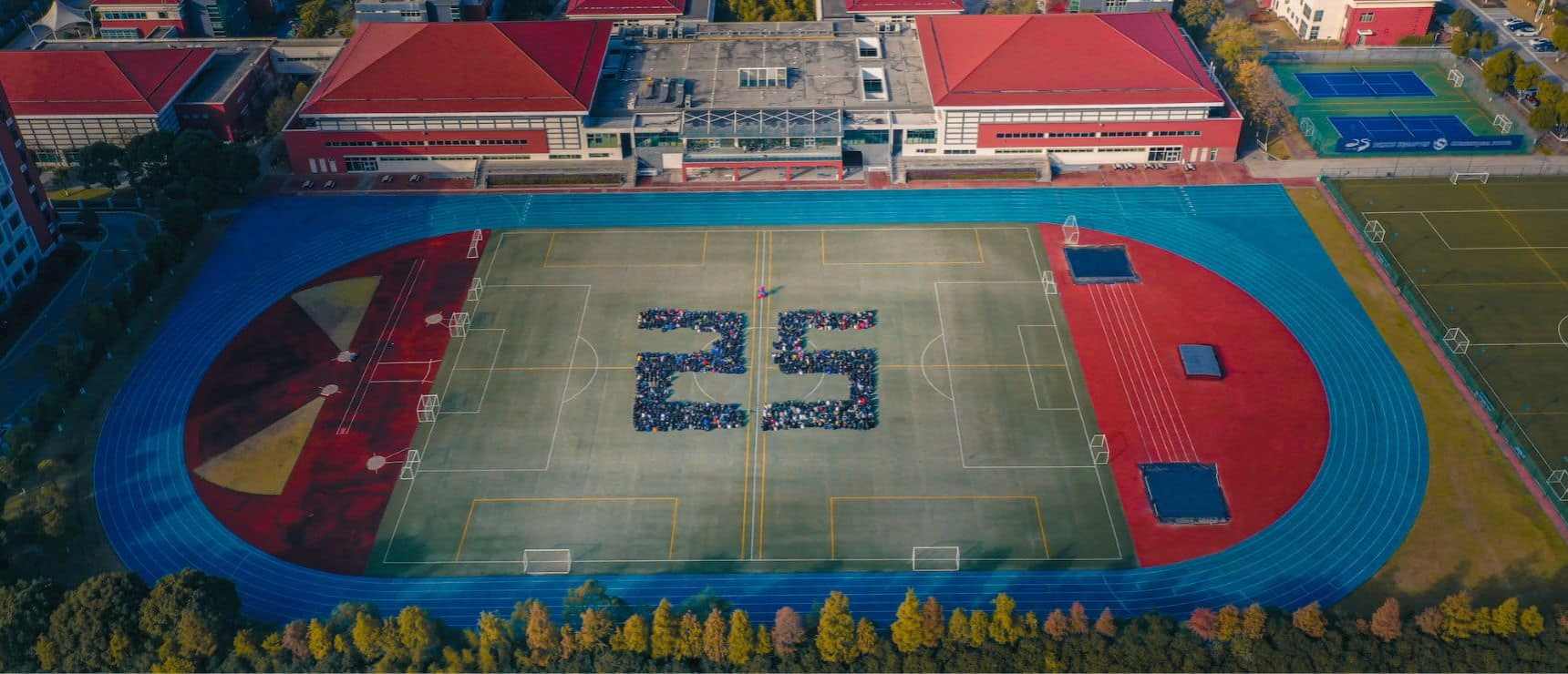 Brightly colored school athletic track and field with students forming the number 25, emphasizing sports and education excellence.