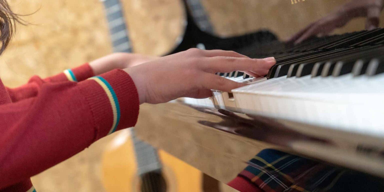 Hands playing piano at a school music class, emphasizing music education and arts in schools.