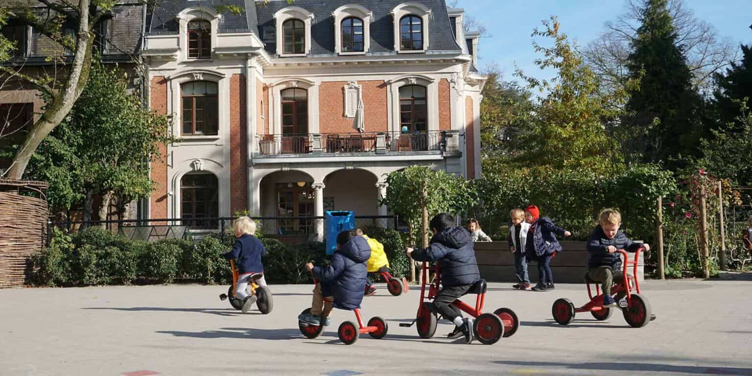 Balcony view of historic European-style school building with children riding bikes outside.