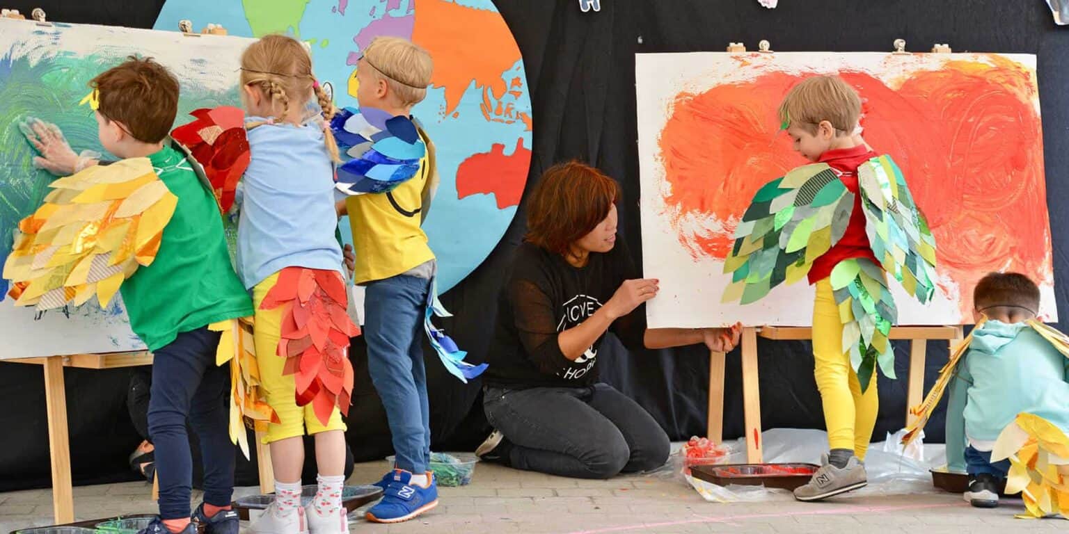 Children dressed in colorful leaf costumes participating in an outdoor art activity at a world school event.