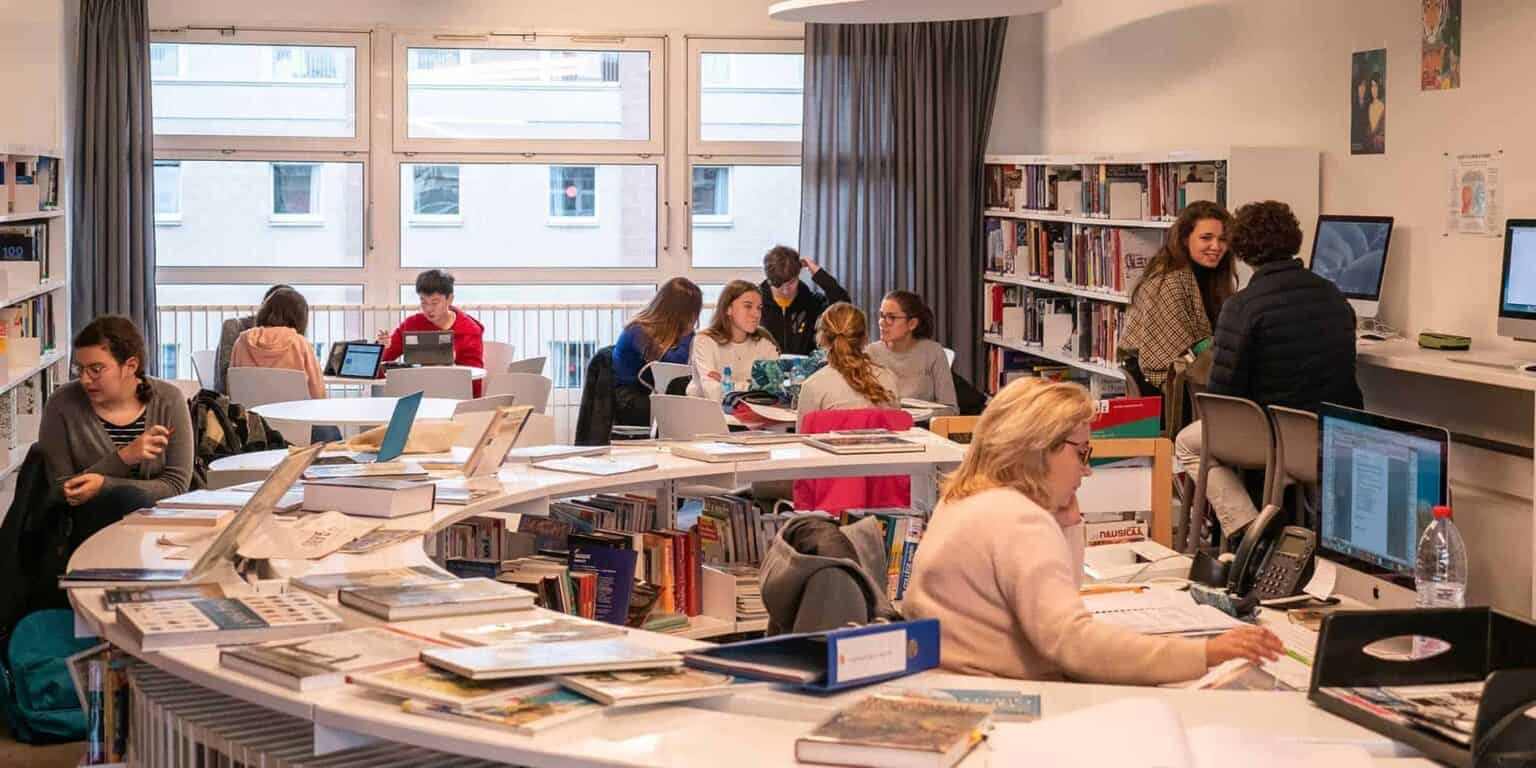 Bright classroom with students studying and working on computers at an international school.