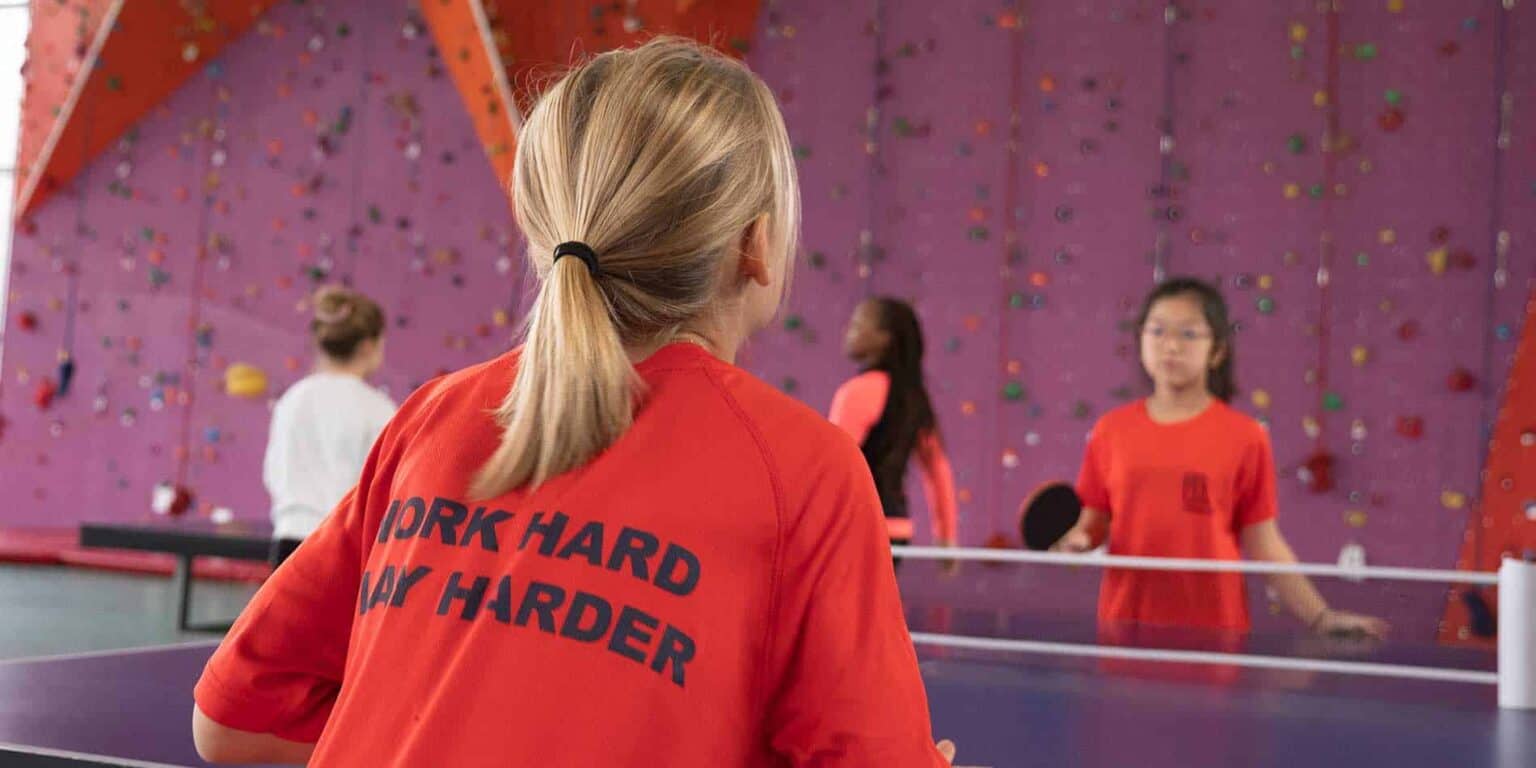 Energetic girl playing table tennis at a vibrant indoor sports facility, showcasing active lifestyle and student engagement.