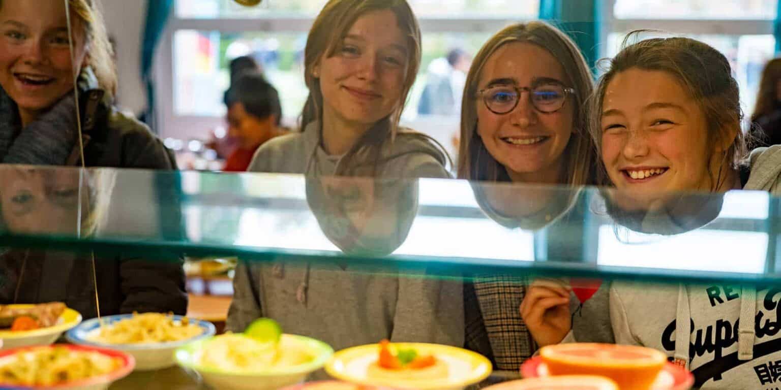 Smiling students looking at food display in school cafeteria, enjoying healthy meals at World Schools.