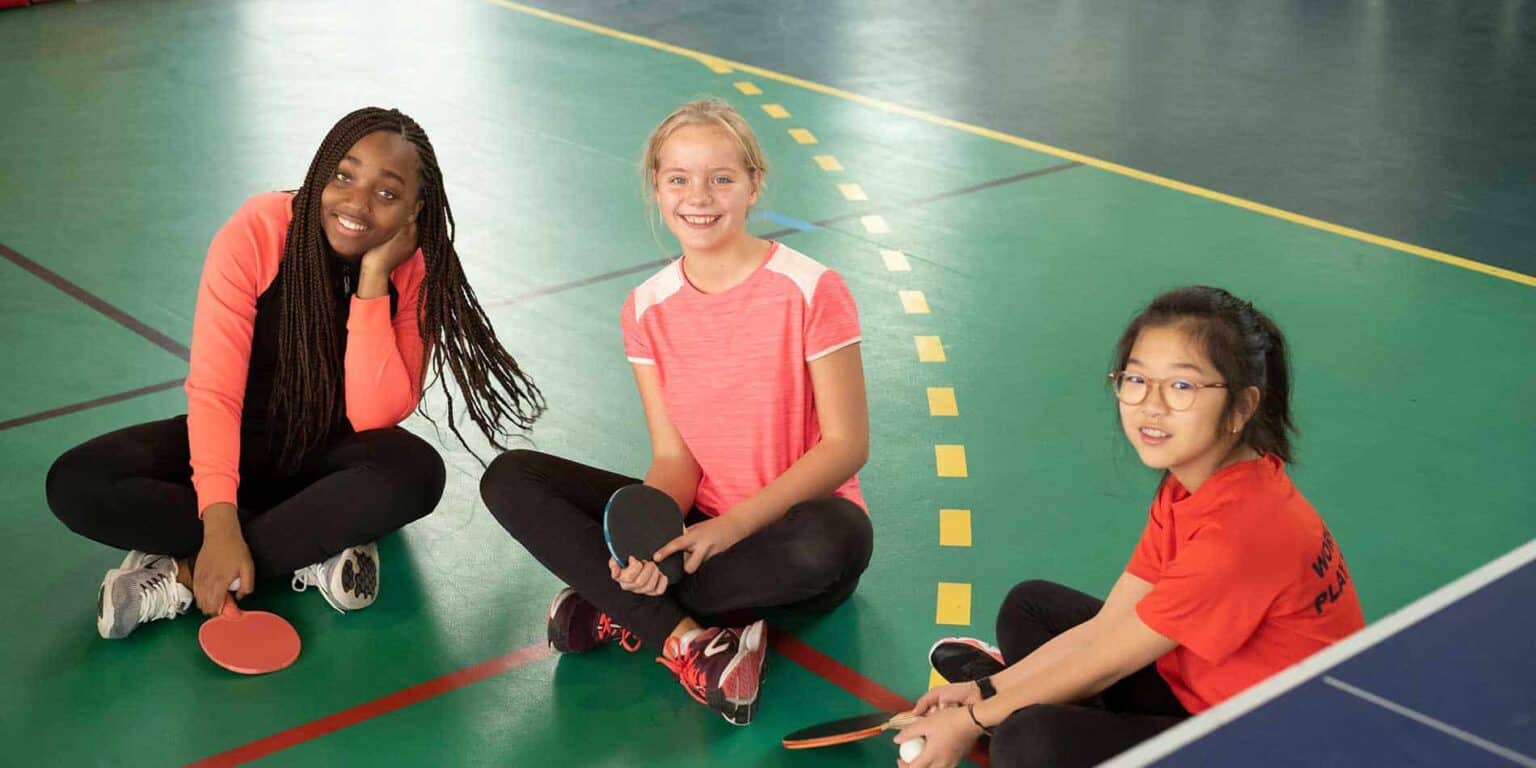 Smiling children playing table tennis on a school sports court, promoting active student lifestyles at World Schools.